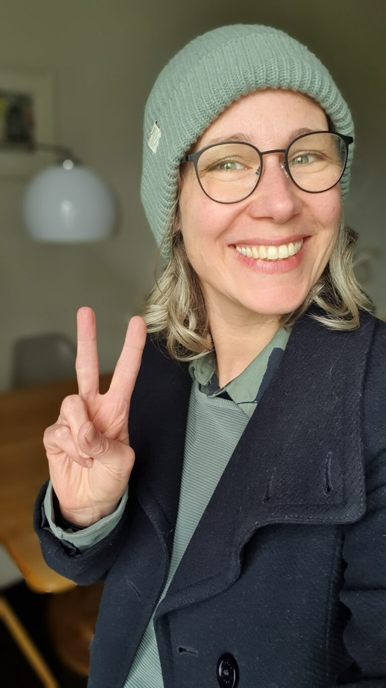 Katja mit Mütze und Brille, lächelnd